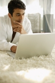 Man in bathrobe, using laptop, hand on chin - Asia Images Group