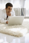 Man in bathrobe, using laptop, hand on chin, smiling - Asia Images Group