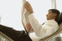 Businessman reclining on chair, reading newspaper - Asia Images Group