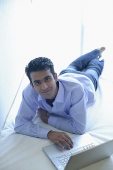 Man lying on bed with laptop, smiling at camera - Asia Images Group