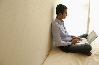 Man sitting cross-legged on bed, using laptop - Asia Images Group