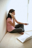 Woman at home, sitting on bed with laptop, using cordless phone - Asia Images Group