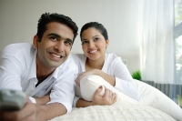 Couple lying on bed, man holding remote control - Asia Images Group