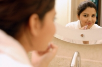 Woman applying lipstick, looking in mirror - Asia Images Group