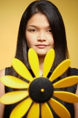 Young woman against yellow background, pin wheel in front of her - Asia Images Group
