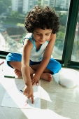 Girl sitting on floor with crayons and paper, pointing to drawing - Asia Images Group
