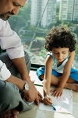 Girl sitting on floor drawing with crayons and paper, father next to her - Asia Images Group