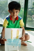 Boy sitting on floor, holding a drawing towards camera - Asia Images Group