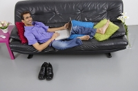 Man sitting on sofa with laptop, smiling at camera - Asia Images Group