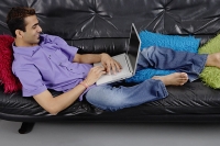 Man lying on sofa using laptop - Asia Images Group
