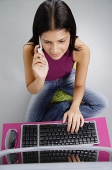 Woman sitting in front of laptop, using mobile phone - Asia Images Group