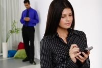 Businesswoman using PDA, man in the background - Asia Images Group