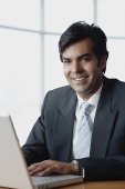 Businessman sitting in front of laptop, looking at camera - Asia Images Group