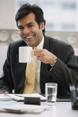 Businessman in office holding mug, smiling - Asia Images Group