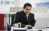 Businessman sitting in office, smiling at camera - Asia Images Group