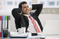 Businessman sitting in office, hands behind head, smiling at camera - Asia Images Group