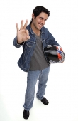 Man carrying motorcycle helmet, looking up at camera, making hand sign - Asia Images Group