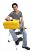 Man sitting on ladder, holding toolbox and drill - Asia Images Group