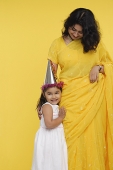 Young girl in white dress and party hat, standing next to her mother - Asia Images Group