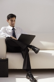 A man sits on a couch with a laptop - Asia Images Group