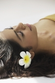 A woman lying down with frangipani flowers around her - Asia Images Group