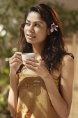 A woman with a flower in her hair drinks a cup of tea - Asia Images Group