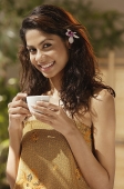 A woman with a flower in her hair drinks a cup of tea - Asia Images Group