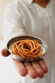 A man holds out a dish of muruku - Asia Images Group