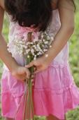A small girl holds flowers behind her back - Asia Images Group