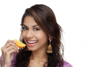 A young woman smiles at the camera as she eats a slice of orange - Asia Images Group