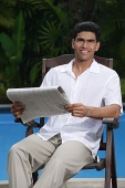 Man sitting in chair holding a newspaper and looking at camera - Asia Images Group