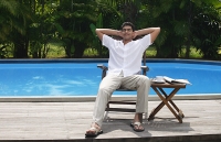 Man relaxing in chair by the pool - Asia Images Group