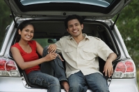 Young couple sitting in car boot smiling at camera - Asia Images Group