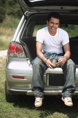 Young man sitting in car boot smiling at camera - Asia Images Group