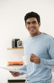 Young man with coffee and paper smiling at camera - Asia Images Group