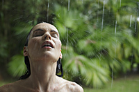 woman standing in tropical rain shower - Alex Mares-Manton