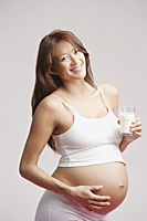 Pregnant woman standing, glass of milk in hand - Alex Mares-Manton