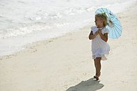 little girl walking on beach under blue umbrella - Alex Mares-Manton