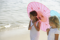 two girls walking on beach under umbrellas - Alex Mares-Manton
