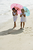 two girls walking on beach under umbrellas - Alex Mares-Manton
