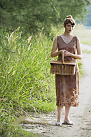 woman on grassy path, holding picnic basket - Alex Mares-Manton