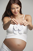 Pregnant woman holding white baby booties - Alex Mares-Manton