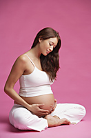 Pregnant woman sitting in half-lotus, hands on stomach - Alex Mares-Manton