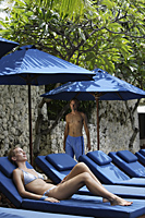 woman in bathing suit on blue lounge chair, man walking - Alex Mares-Manton