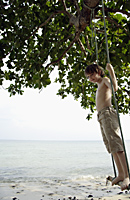 Boy standing in swing near ocean - Alex Mares-Manton