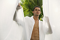 Man standing between open white curtains - Alex Mares-Manton