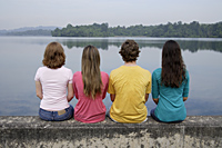 Group of teens sitting on wall next to lake - Nugene Chiang