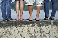 legs of teens standing on wall near lake - Nugene Chiang