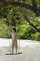 Boy standing on swing on beach - Alex Mares-Manton