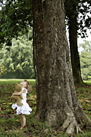 Little girl holding teddy bear, looking up at tree - Alex Mares-Manton